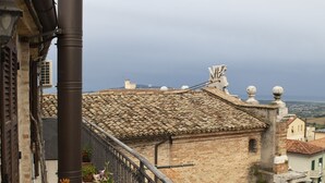 A balcony with a metal railing, potted plants, and a view of the town below. - B&B Porta Marina (Recanati)