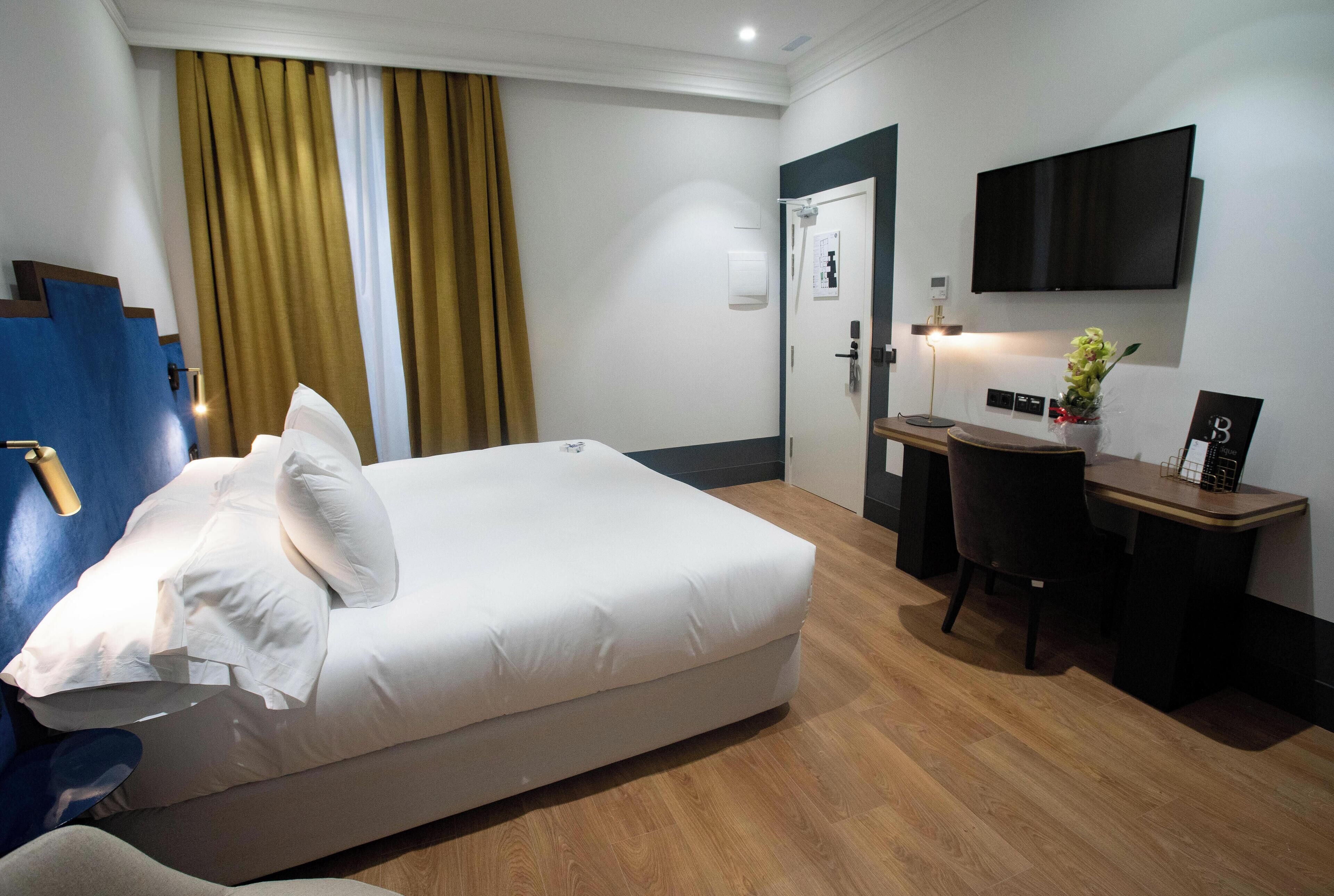 Una habitación de hotel con cama, escritorio, silla, televisor y puerta.