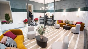 A hotel lobby with a reception desk, seating areas, and decorative plants. - Soho Boutique Congreso (Madrid)