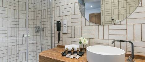 A modern bathroom with a herringbone tile pattern, a wooden vanity, a round sink, a mirror, and a shower area.