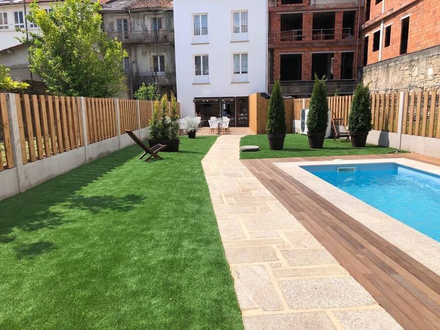 Un patio con césped artificial, una terraza de madera y una piscina.