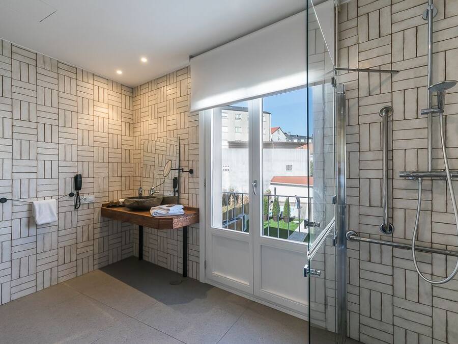 A modern bathroom with a geometric tile backsplash, a wooden vanity, a glass shower enclosure, and a view of the outside.