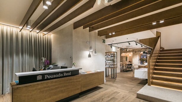 A reception area with a wooden reception desk, a staircase, and a seating area. - Hotel Pousada Real (Caldas de Reis)