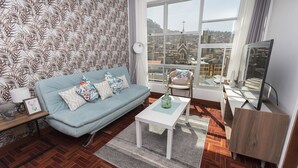 Sala de estar moderna com um sofá azul, uma mesa de centro branca e uma grande janela com vista para a cidade.