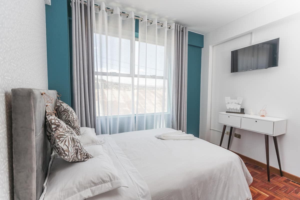 A hotel room with a bed, a desk, a TV, and a window with curtains.