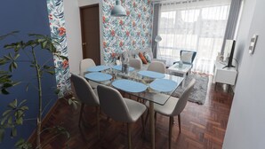 Uma área de jantar com mesa de vidro, cadeiras e papel de parede floral.