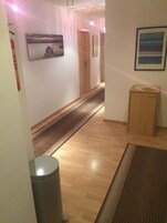 Um corredor com piso de madeira, uma lixeira e duas portas.