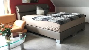 Un dormitorio moderno con cama, una mesita de vidrio, un sofá y una pared de acento roja.