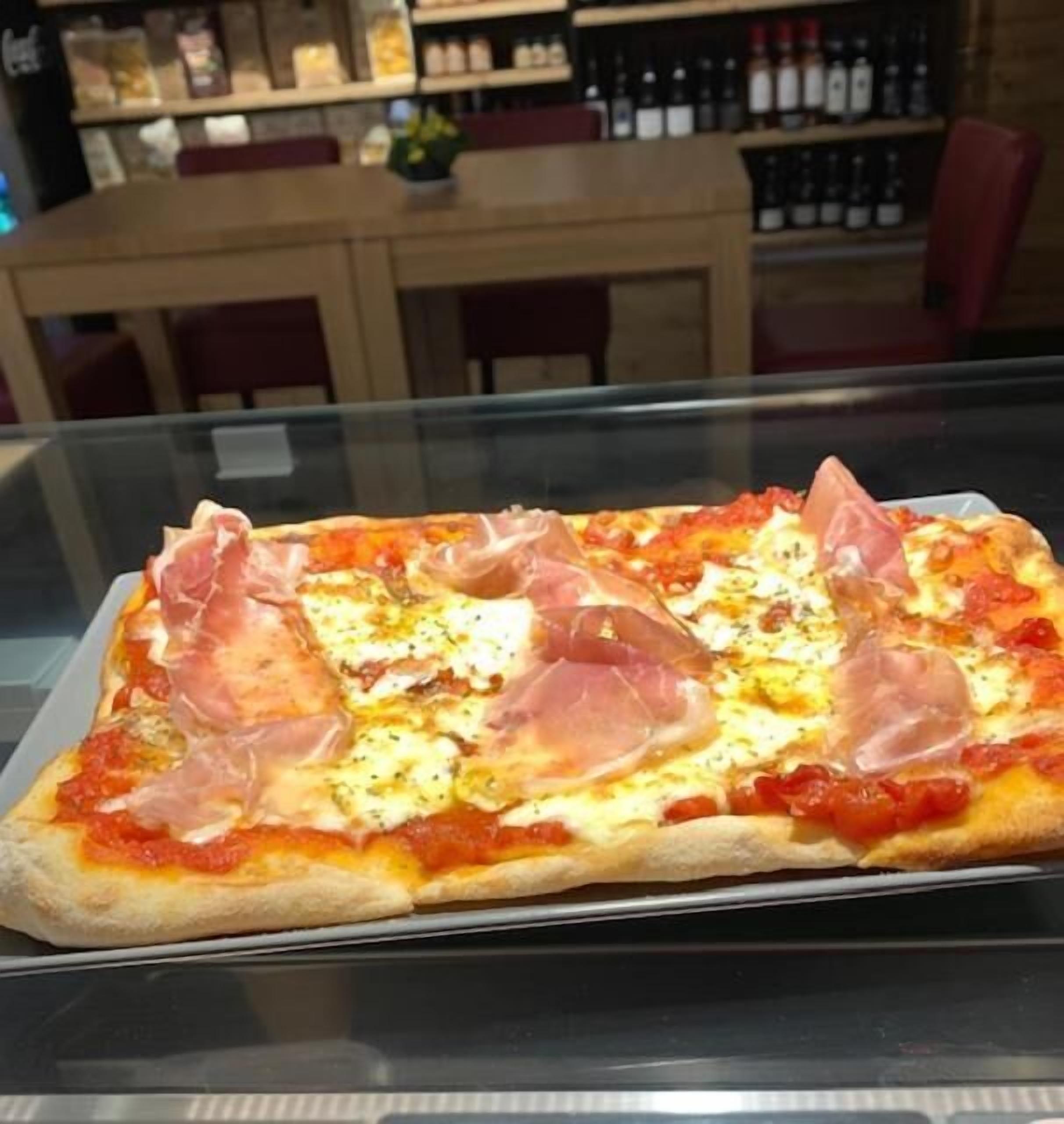 Uma pizza com presunto e queijo em uma vitrine de vidro.