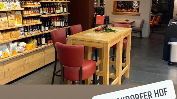 Una tienda de Panini con estantes llenos de bocadillos y bebidas, una mesa de madera con sillas rojas y una chimenea al fondo.