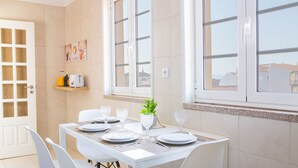 A dining area with a table set for four, a window with a view of buildings, a toaster on a shelf, and a plant on the windowsill. - Praça 44 Boutique Apartments (Braga)