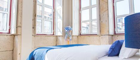 Una stanza con un letto, un manichino e ampie finestre con infissi rossi.