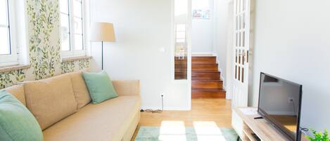 A living room with a sofa, a TV, a lamp, and a staircase leading to another room.