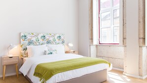 A bedroom with a bed, two bedside tables, a nightstand, a window, and a view of buildings outside. - Praça 44 Boutique Apartments (Braga)