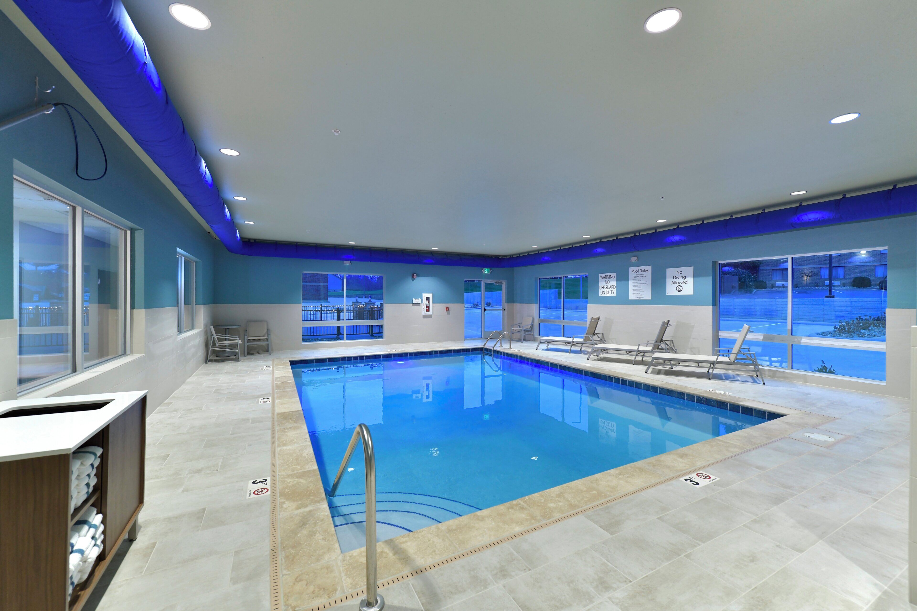 Piscina com água cristalina, rodeada por espreguiçadeiras e piso cerâmico.