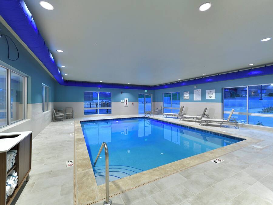 A swimming pool with clear water, surrounded by lounge chairs and a tiled floor.