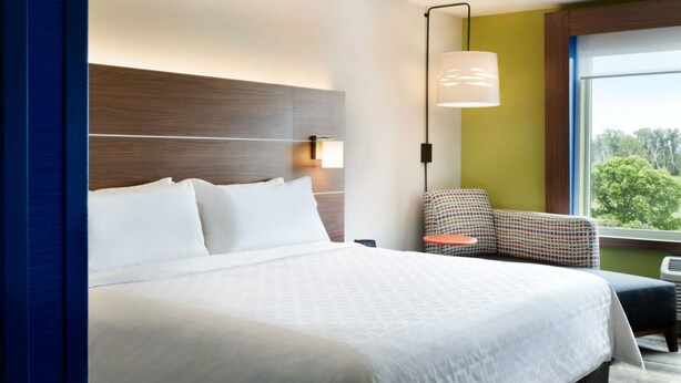 A hotel room with a large bed, a nightstand, a chair, and a window with a view of trees. - Holiday Inn Express & Suites Millersburg by IHG (Millersburg)