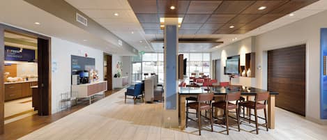 Un interior de cafetería moderno con techo de madera, una mesa central para comer con sillas y una máquina de espresso a la vista.