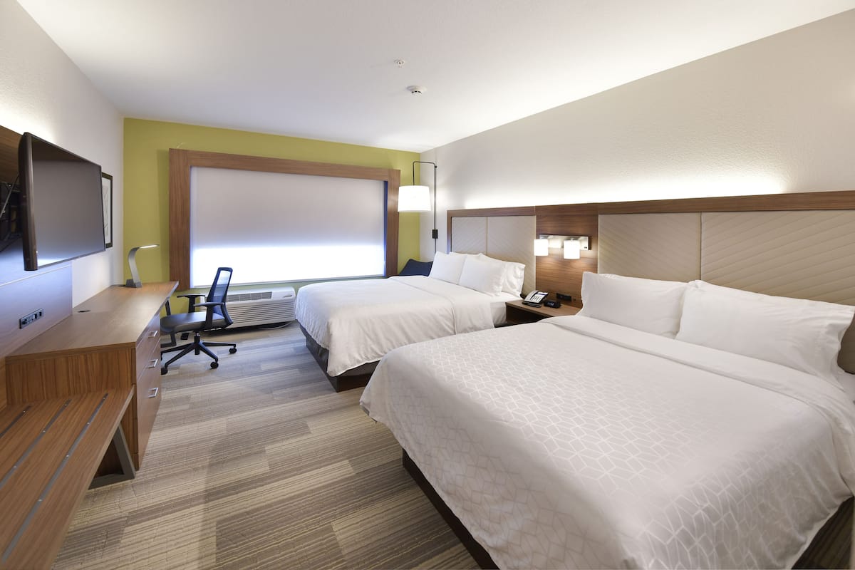 A hotel room with two beds, a desk, a chair, a TV, and a window with blinds.