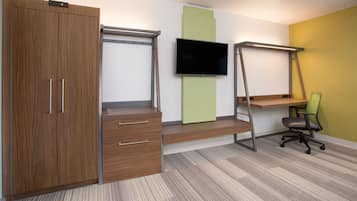 A bedroom with a wooden wardrobe, a desk with a chair, a TV mounted on the wall, and a green accent wall.
