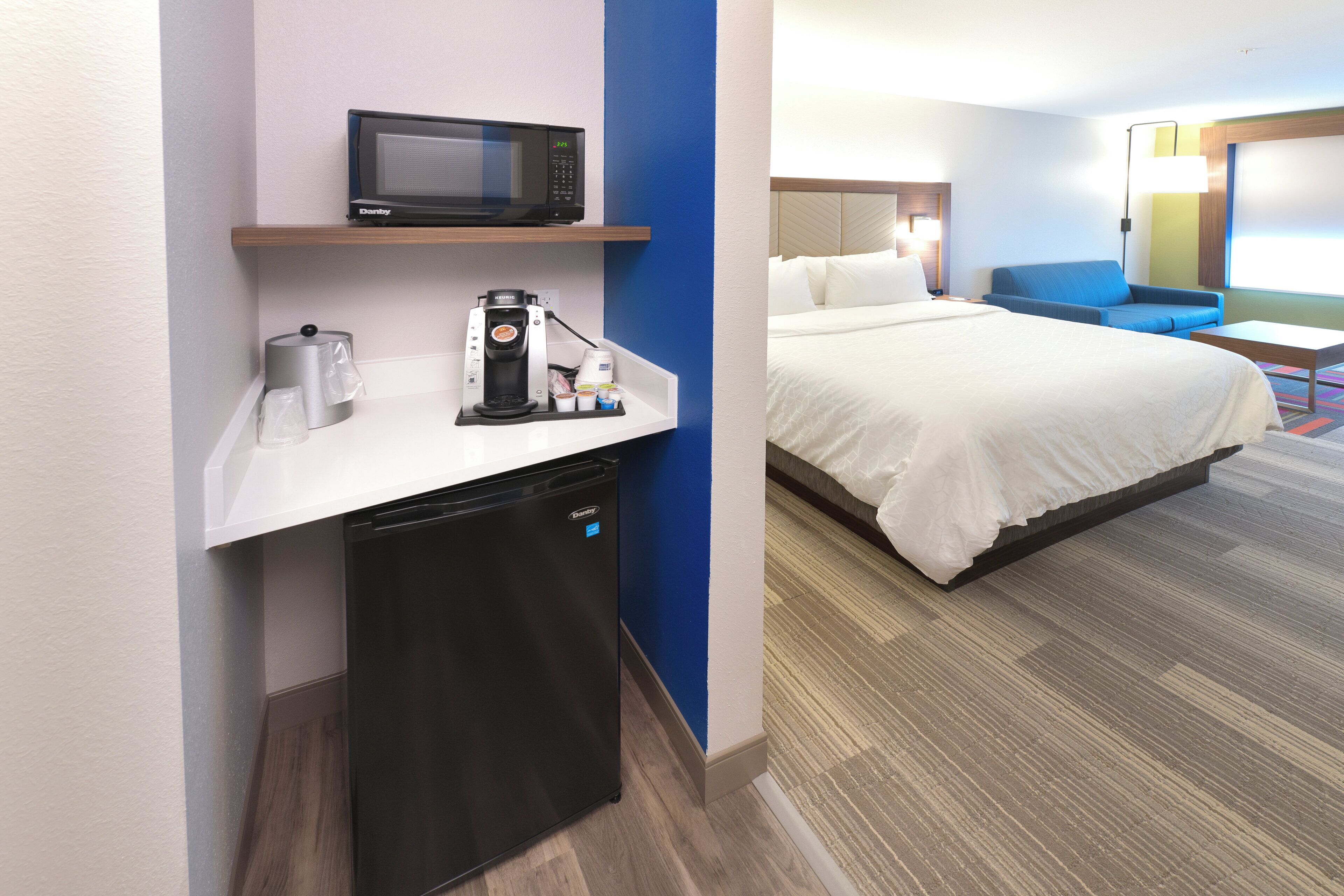 A hotel room with a bed, a desk with a microwave, a coffee maker, and a mini-fridge.