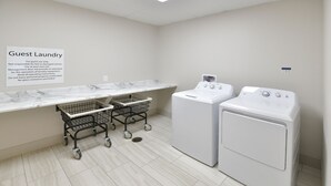 A guest laundry area with two washing machines, a marble countertop, and two shopping carts. - Holiday Inn Express & Suites Millersburg by IHG (Millersburg)