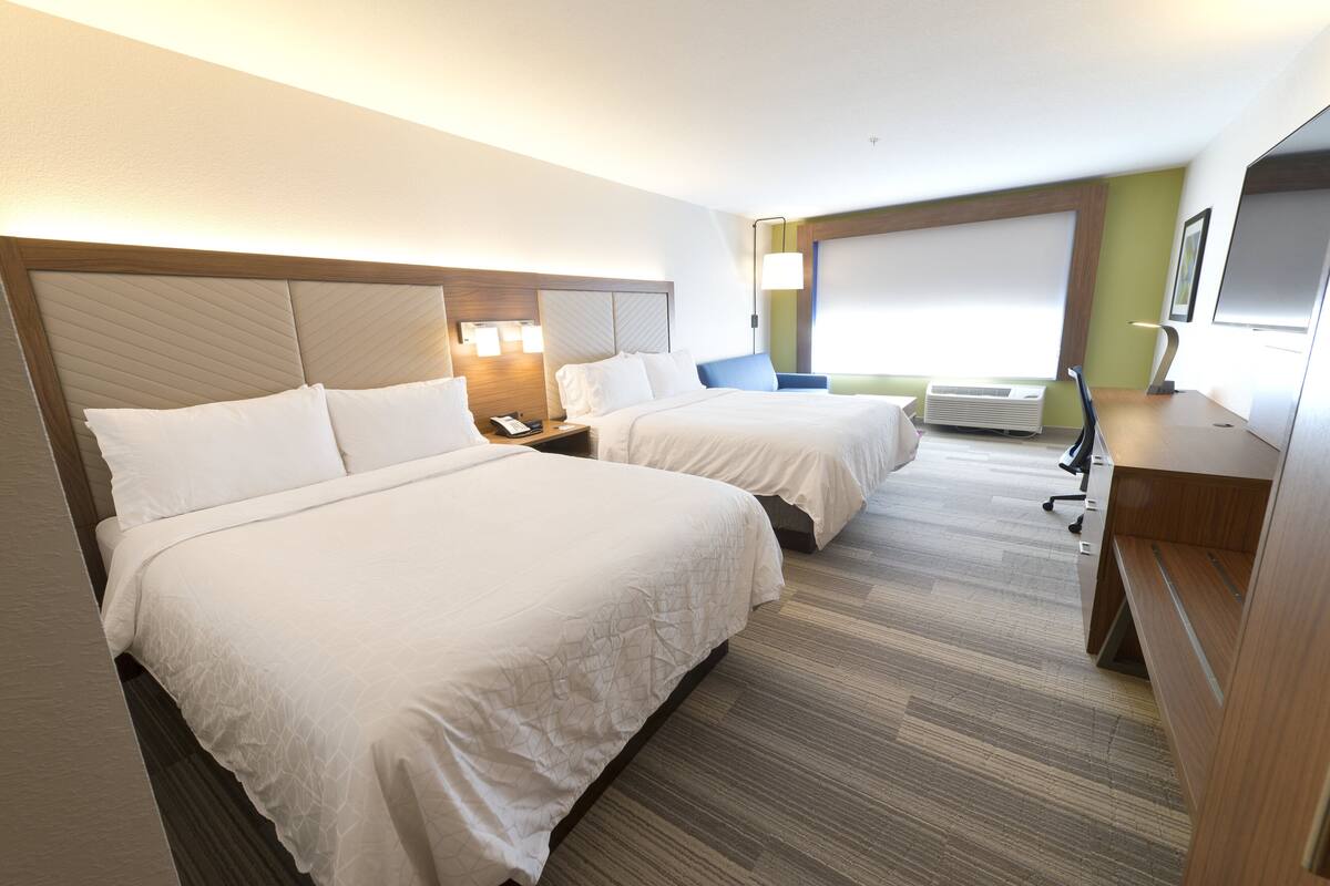 A hotel room with two beds, a desk, a chair, and a large window.