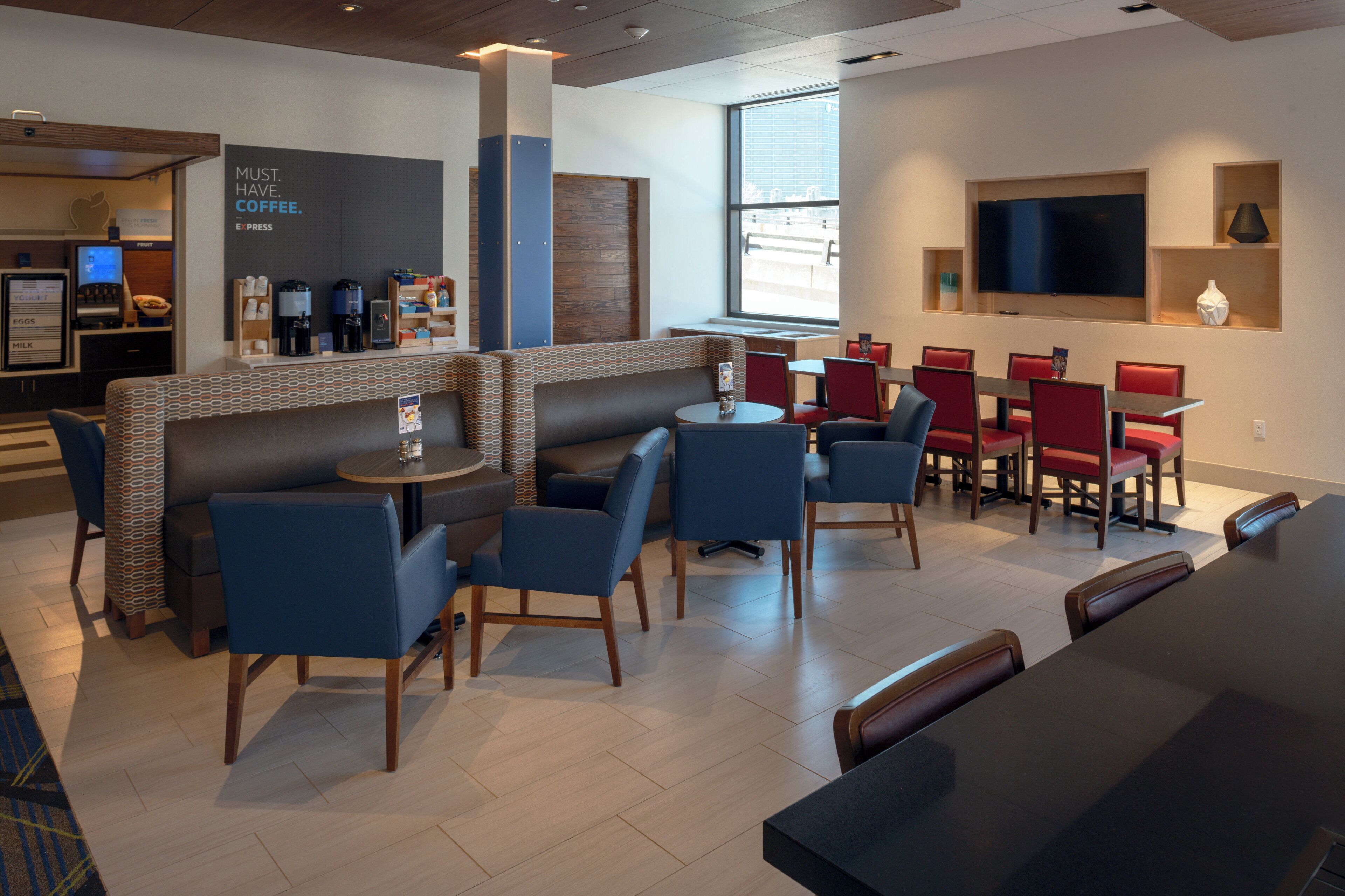 A modern cafe with seating arrangements, a coffee station, and a large window providing natural light.