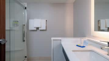 A bathroom with a glass shower enclosure, a white sink, and a towel rack with two towels.
