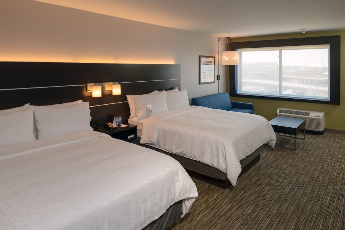 A hotel room with two beds, a nightstand, a desk, and a large window.