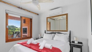 A hotel room with a bed, a large mirror, a ceiling fan, and a window with a view of greenery. - San Lameer Villa Rentals 10413 (Southbroom)