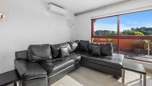A black leather sectional sofa with a glass table and a view of greenery outside. - San Lameer Villa Rentals 10413 (Southbroom)
