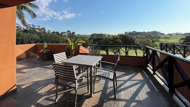 A balcony with a table and chairs, overlooking a scenic landscape with trees and a clear sky. - San Lameer Villa Rentals 10413 (Southbroom)