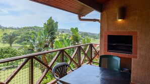 Een balkon met uitzicht op een weelderig landschap, een barbecue en een tafel met stoelen.