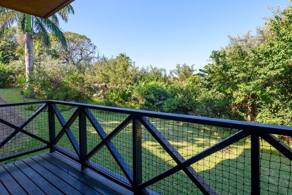 A wooden deck with a metal railing overlooking a grassy area with trees.