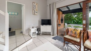 A modern living room with a television, wicker chairs, a white cabinet, and a view of greenery outside. - San Lameer Villa Rentals 2204 (Southbroom)