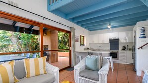 A spacious living area with a sofa, wicker chairs, and a dining table. A kitchen with white cabinets and a built-in oven is visible. - San Lameer Villa Rentals 2408 (Southbroom)
