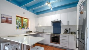 A modern kitchen with white cabinets, a stainless steel oven, and a large window with a view of greenery. - San Lameer Villa Rentals 2408 (Southbroom)