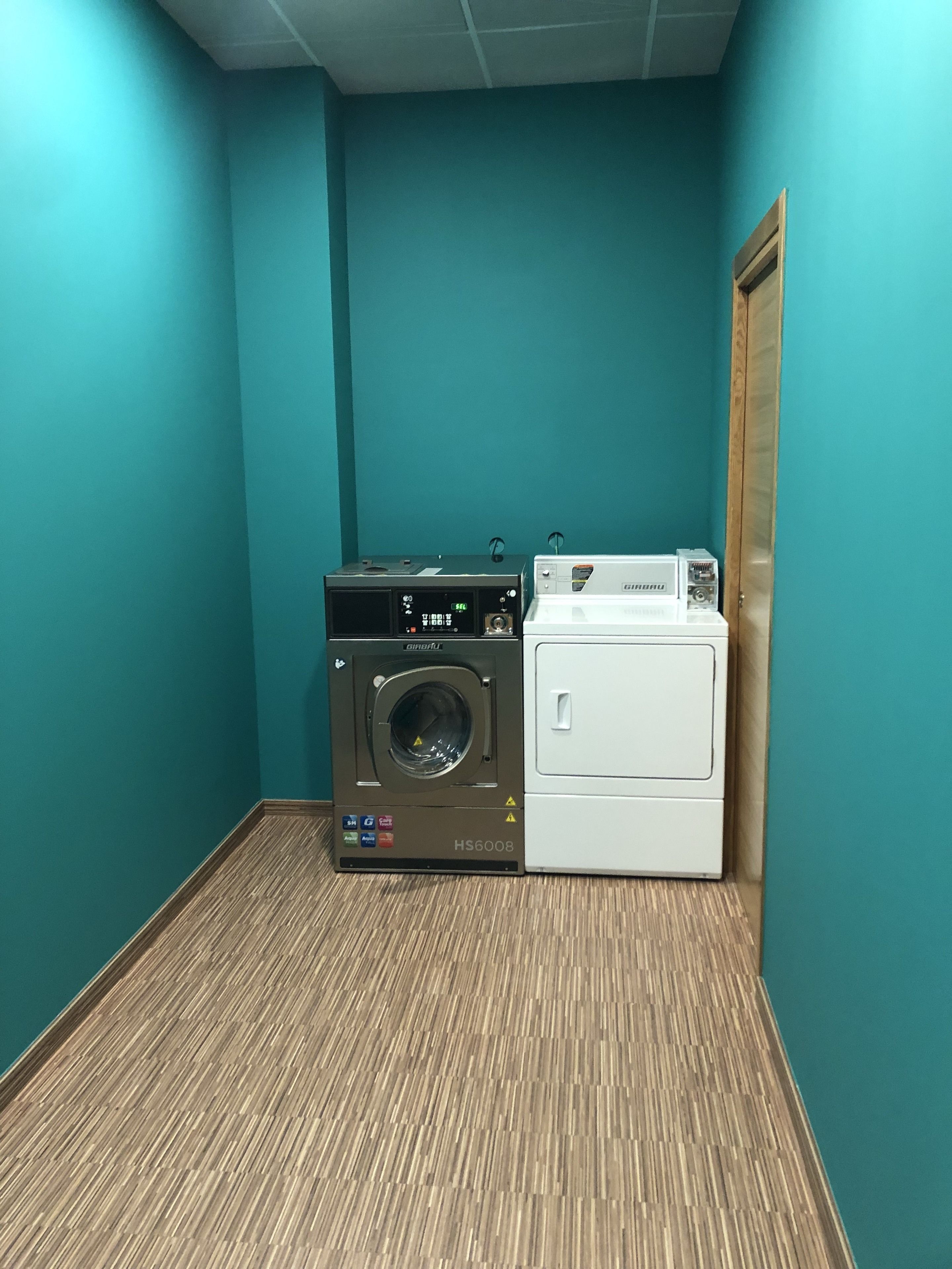 A laundry room with a front-loading washer and dryer, teal walls, and a wooden floor.