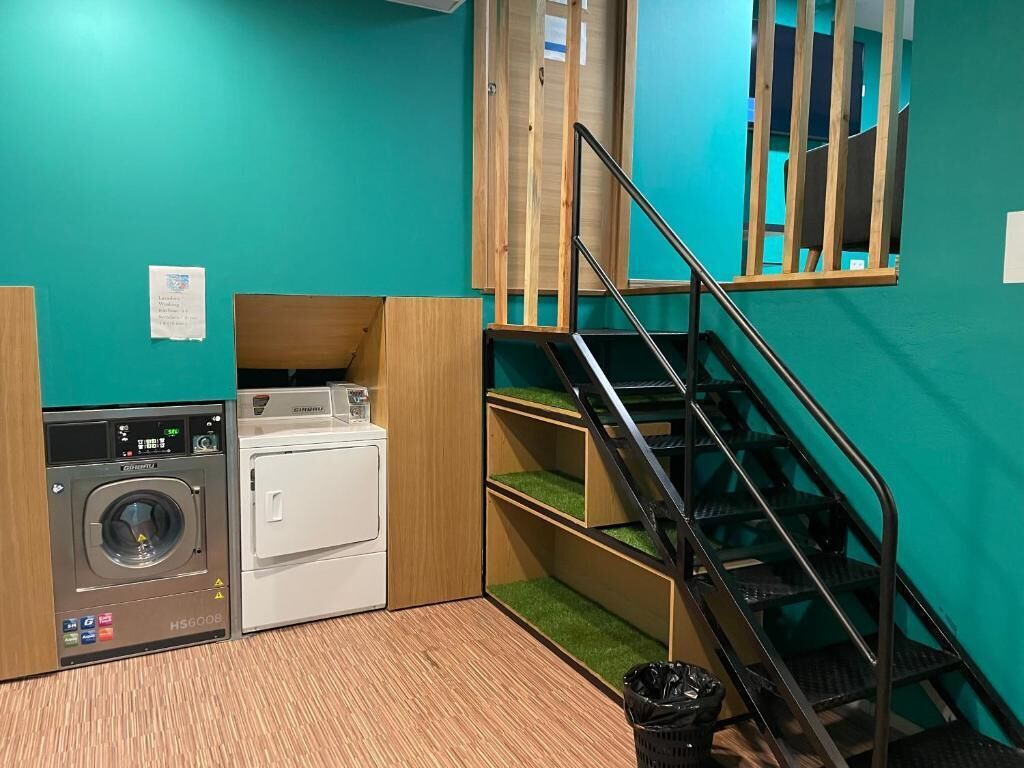 Un cuarto de lavandería con lavadora, secadora y un cubo de basura pequeño.