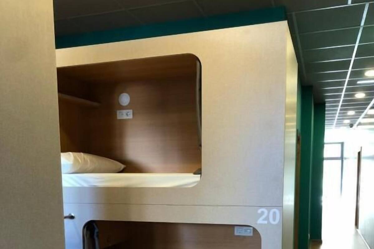 Uma cama beliche com o número '20' na lateral, piso de madeira e uma parede verde ao fundo.