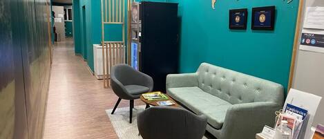 Una moderna zona de recepción con decoración en tonos verde azulado, un mapa mundial en la pared, un sofá gris, dos sillones y un mostrador de recepción con folletos informativos.