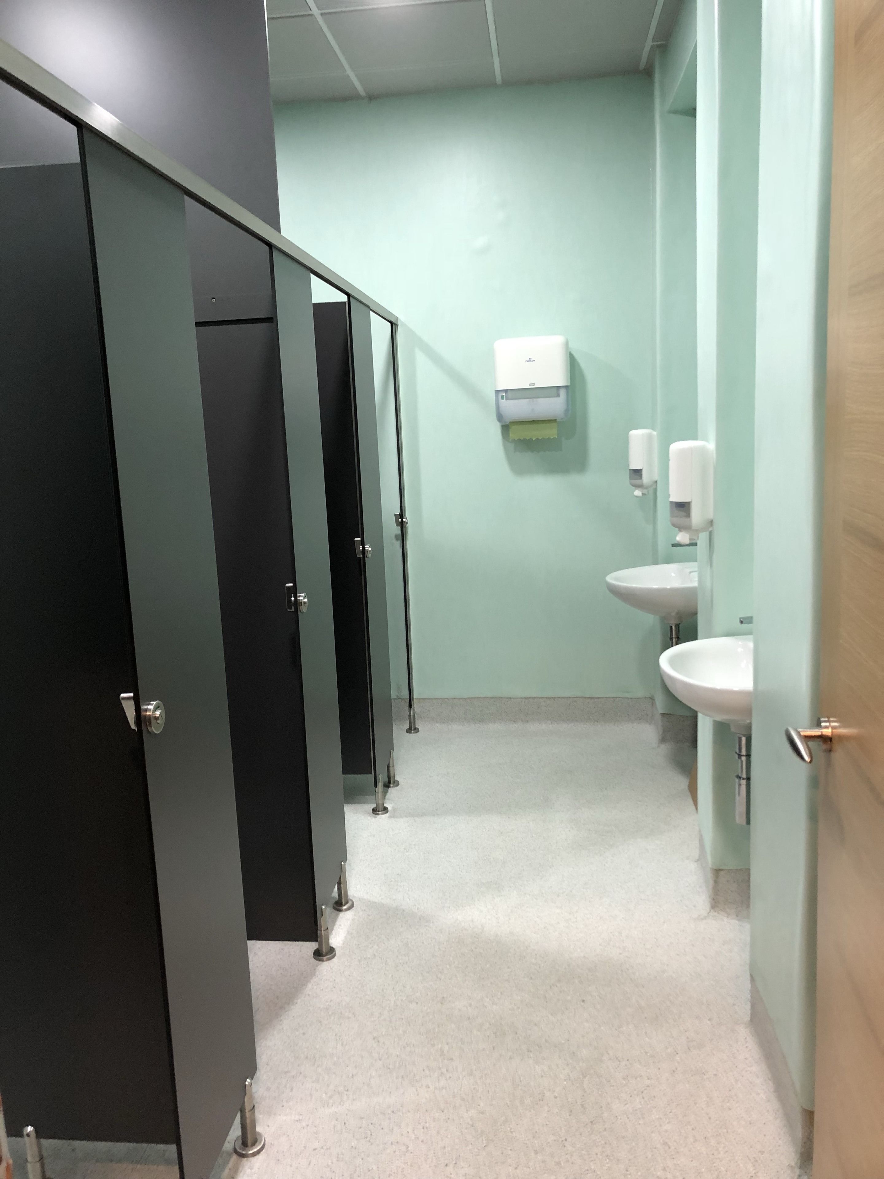 Un baño con varios cubículos, un secador de manos y lavamanos.
