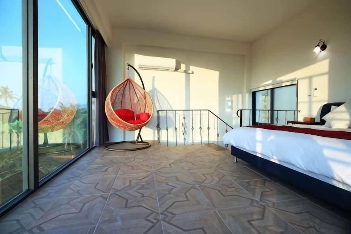 Een slaapkamer met een hangstoel, een bed, een balkon met uitzicht en een trap.