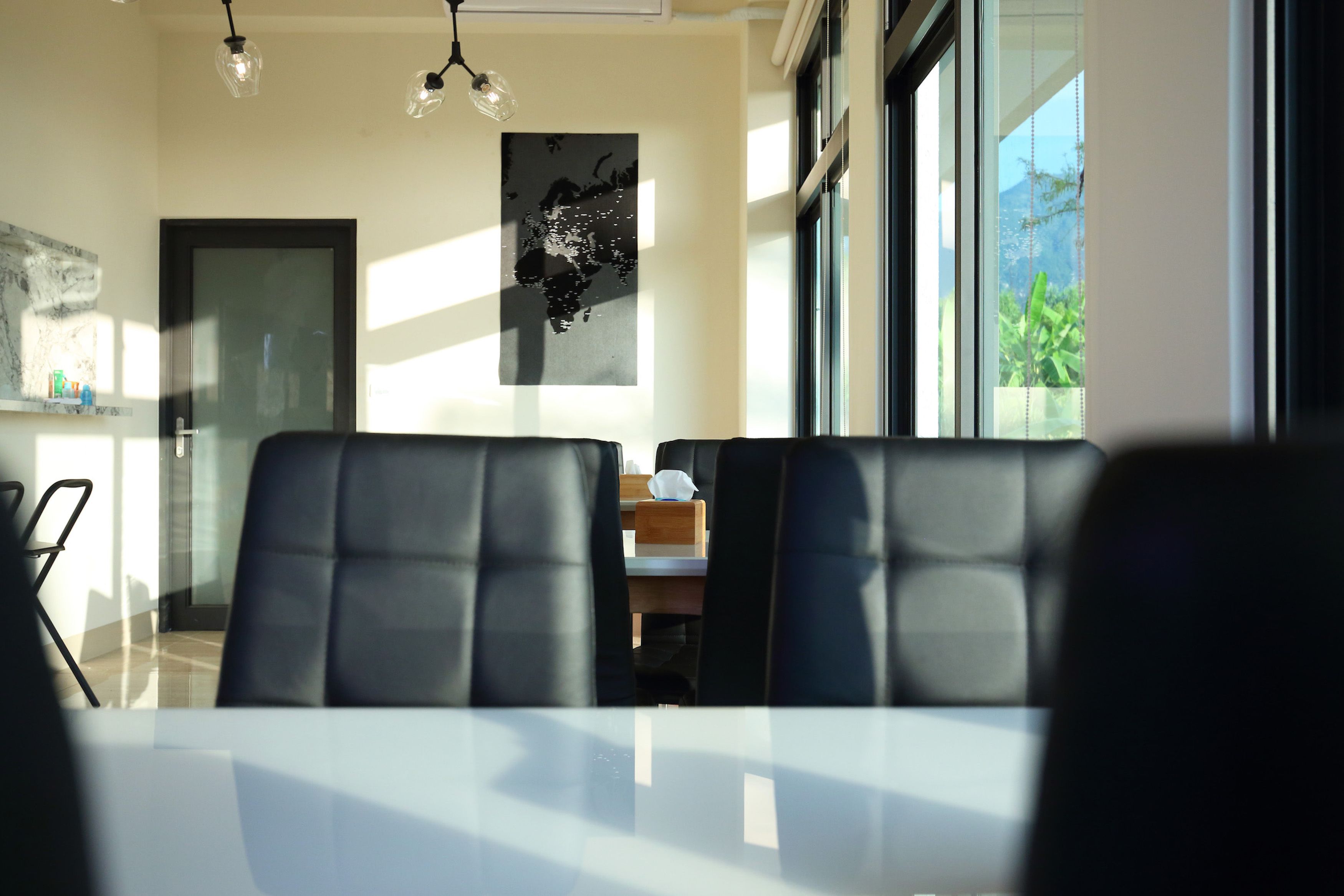 Un comedor con una mesa y sillas, un mapa del mundo en la pared y vistas al exterior de vegetación.
