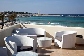 A terrace with white wicker furniture, a view of the sea, and a distant lighthouse. - Miraspiaggia (San Vito Lo Capo)