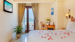 Une chambre d’hôtel avec un lit, un bureau, une chaise, une plante en pot et une vue sur la mer, visible par la porte.