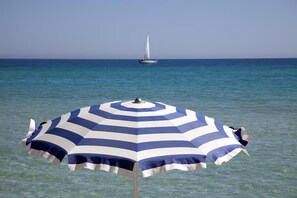 A beach umbrella with a sailboat in the background. - Miraspiaggia (San Vito Lo Capo)