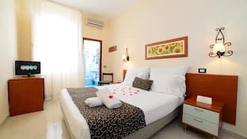 Habitación de hotel con una cama, un televisor sobre un soporte de madera, una mesita de noche y una lámpara fijada a la pared.
