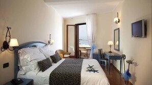 Une chambre d’hôtel avec un lit, des lampes de chevet, un bureau, une chaise, une télévision et une vue sur la mer.